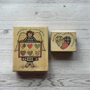Könnte beinhalten: Zwei Holzstempel mit Herzmotiven. Einer zeigt einen Engel, der ein Patchwork-Herzdesign mit dem Text "Give God the pieces... He will patch together" hält. Der andere sagt "Piece by piece... a bit of thee... a bit of me."