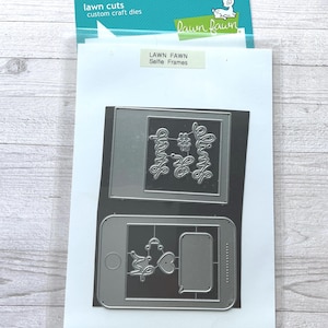 Puede incluir: Troqueles personalizados Lawn Fawn Selfie Frames. El paquete contiene troqueles de corte de metal con forma de smartphone y marco rectangular. Los troqueles incluyen las palabras "Selfie" y otros elementos decorativos.
