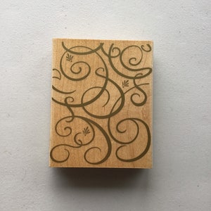 May include: A wooden stamp with a design of gold swirls and flourishes. The stamp is rectangular and has a light brown color.