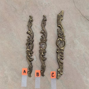 May include: Three ornate gold-toned metal decorative pieces with intricate floral designs. The pieces are labeled A, B, and C.