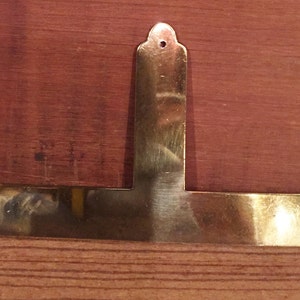 May include: A gold-coloured metal corner brace with a T-shape and decorative edges.