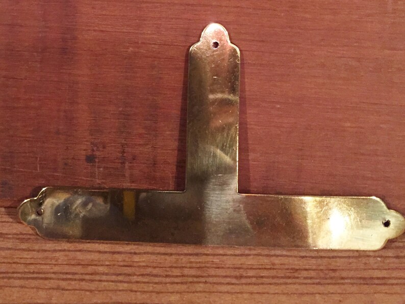 May include: A gold-coloured metal corner brace with a T-shape and decorative edges.