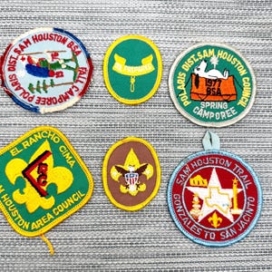 May include: Six embroidered Boy Scouts of America patches. Top row: Sam Houston BSA Fall Camporee, Be Prepared, and 1977 BSA Spring Camporee with Snoopy. Bottom row: El Rancho Cima Sam Houston Area Council, a brown eagle emblem, and Sam Houston Trail.