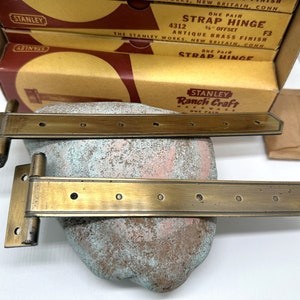 May include: Two antique brass strap hinges with a Stanley Ranch Craft Hardware label. The hinges are 1/2 inch offset and have a satin finish.