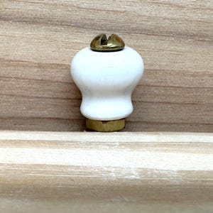 May include: White ceramic cabinet knob with a brass screw and base. The knob has a rounded top and a flared base. This hardware is suitable for drawers and cabinets.