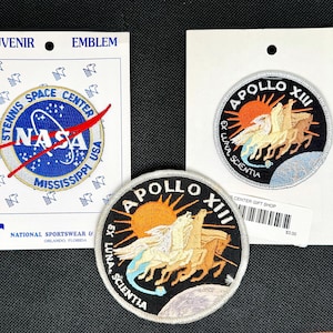 May include: Three embroidered patches including a circular Stennis Space Center NASA emblem on a white card, and two circular Apollo XIII patches featuring a sun, horses, and the text Ex Luna Scientia, with one patch attached to a white card.