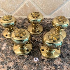 May include: Six brass door knobs with a floral design. Each knob has a round base and a raised flower design on the top.