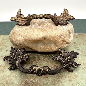 May include: Two ornate, antique-style cabinet pulls with a leaf design. The pulls are made of metal and have a dark bronze finish.