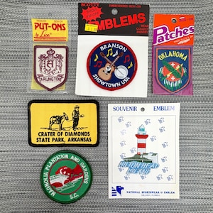 May include: A collection of six embroidered patches featuring various designs including an Arlington crest, a Branson Showtown USA guitar and banjo, an Oklahoma state emblem, a Crater of Diamonds State Park patch, a Magnolia Plantation patch, and a lighthouse.
