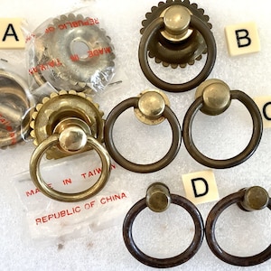 May include: Assortment of antique brass cabinet knobs with different styles and finishes. Some knobs have a decorative ring around the base, while others have a simple design. The knobs are made in Taiwan and the Republic of China.