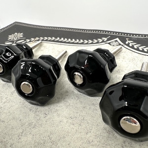 May include: Set of four black faceted cabinet knobs with silver-tone metal hardware. The knobs have a glossy finish and a geometric design. These decorative knobs are suitable for drawers and cabinets.