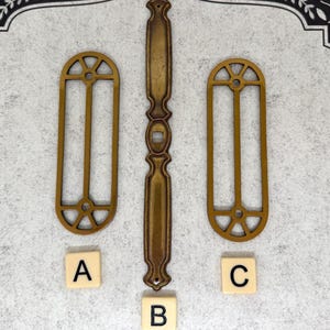 May include: Three antique brass-toned metal decorative pieces. Two are arched window-shaped, and one is a long, ornate handle. Lettered tiles A, B, and C are below the objects. The background is a light gray with a decorative black border.