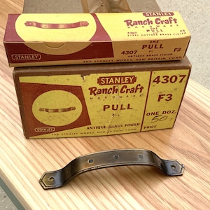 May include: Two boxes of Stanley Ranch Craft hardware with antique brass pulls. The boxes are yellow with red and black lettering. The top box says "One Pull 4 1/2" and the bottom box says "One Doz. 50¢ Price".