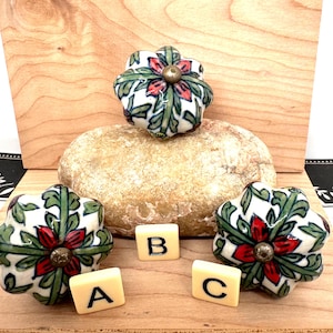 May include: Three floral ceramic cabinet knobs with a white background, red and green floral design, and brass hardware. Three letter tiles spell out the letters A, B, and C.