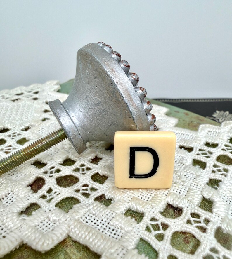 Może przedstawiać: Biały ceramiczny kubek z czarnym uchwytem i napisem "But First, Coffee" pogrubioną, czarną czcionką. Kubek jest ustawiony na rozmytym tle, sugerującym przytulne otoczenie.