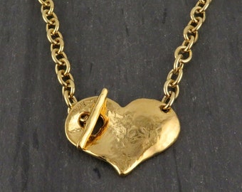 May include: A gold-colored necklace featuring a heart-shaped pendant. The pendant has a textured surface and is connected to a chain. The necklace has a toggle clasp. The chain is approximately 18 inches long.