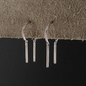 May include: A pair of silver hoop earrings with dangling silver bars. The earrings are simple and elegant.