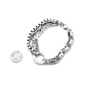May include: Silver-toned bracelet featuring a multi-chain design with a variety of link styles. The bracelet includes a square link chain, a classic chain, and a larger, studded chain. A dime is included for size reference.