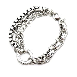May include: Silver-toned bracelet featuring a multi-chain design. The bracelet includes a square link chain, a delicate chain, and a larger chain with rivet details. It has a hammered ring detail and a lobster clasp closure.