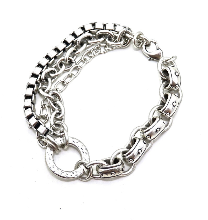 May include: Silver-toned bracelet featuring a multi-chain design. The bracelet includes a square link chain, a delicate chain, and a larger chain with rivet details. It has a hammered ring detail and a lobster clasp closure.