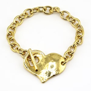 May include: Gold-tone bracelet featuring a hammered heart pendant and a toggle clasp. The bracelet has a chunky chain design. The heart pendant is approximately 1.5 inches wide.