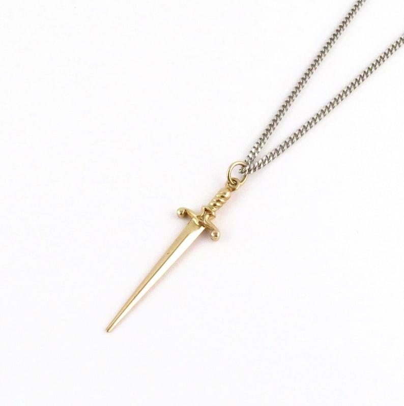 Peut inclure: Un collier avec un pendentif en forme de dague dor&eacute;e et une cha&icirc;ne en argent.