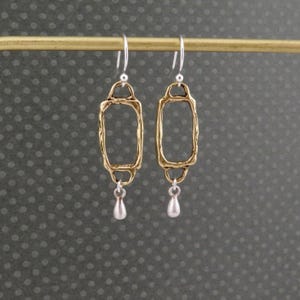 Op de afbeelding: Gouden en zilveren oorhangers met een rechthoekig frame en een traanvormige hanger.