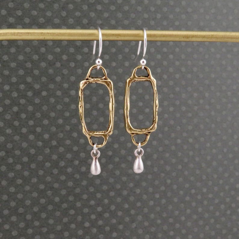 Op de afbeelding: Gouden en zilveren oorhangers met een rechthoekig frame en een traanvormige hanger.