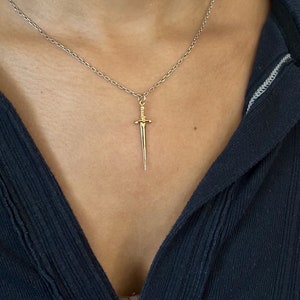 Peut inclure: Un collier en cha&icirc;ne argent avec un pendentif en forme de dague dor&eacute;e.