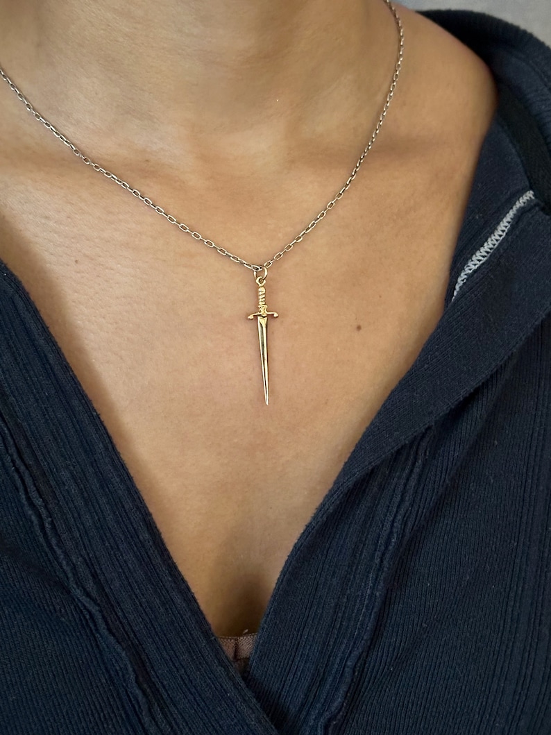 Peut inclure: Un collier en cha&icirc;ne argent avec un pendentif en forme de dague dor&eacute;e.