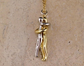 May include: A gold and silver necklace with a pendant of two figures embracing. The figures are intertwined and form a circle.