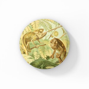 May include: Round decorative item featuring a vintage illustration of two chameleons in a jungle setting. The chameleons are depicted in shades of brown and tan, surrounded by green and yellow foliage. The design is printed on a white background.