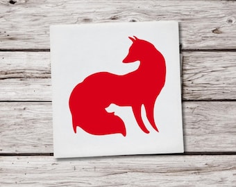 May include: A red fox silhouette on a white square. The fox is depicted in a side profile, with its tail curled. The image is set against a weathered, light-colored wooden background. The design is simple and bold.