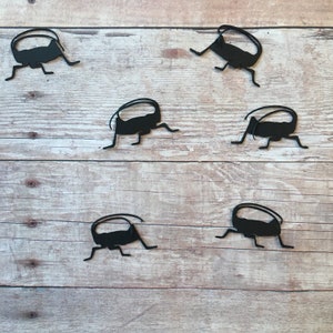 May include: Six black metal cricket silhouettes on a light brown wood background.
