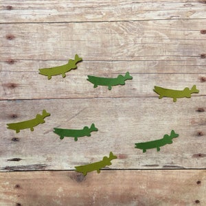 May include: Six green paper alligator cutouts on a wood background. The alligators are all facing the same direction and are arranged in a semi-circle.