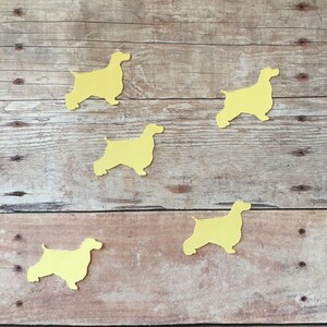 May include: Five yellow paper cutouts of cocker spaniel silhouettes on a wood background.