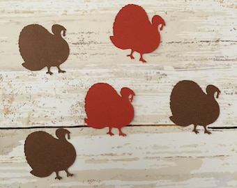 May include: Five paper cutouts of turkeys, two are brown and three are orange. The turkeys are arranged in a row on a white wooden background.