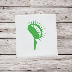 May include: A green Venus flytrap illustration on a white square. The plant is depicted in a minimalist style, with a detailed trap and stem. The background is a wooden surface.