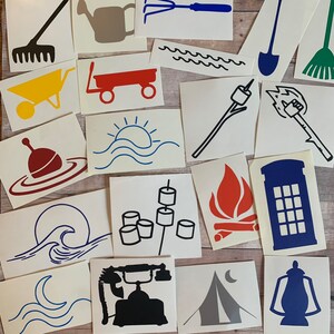 May include: A set of 16 camping and outdoor themed stickers. The stickers are on white paper and feature various designs, including a campfire, a tent, a phone booth, a wave, a rake, a wagon, a sun, a marshmallow on a stick, a lantern, a shovel, a broom, a watering can, a garden rake, a buoy, and a wave.