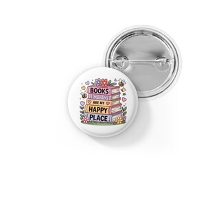 May include: A white button pin with a colorful design featuring a stack of books, flowers, hearts, and bees. The text on the pin reads "BOOKS ARE MY HAPPY PLACE."
