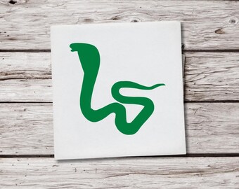 May include: A square white sticker featuring a green cobra snake design. The snake is stylized with a curved body and raised head, set against a light wood grain background.