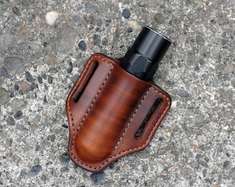 May include: A brown leather holster for a flashlight. The holster has a stitched design and a flap that secures the flashlight.