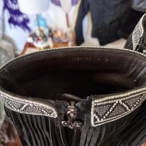 May include: Close-up of a black leather boot with fringe and a decorative beaded trim around the top. The interior shows the text "DENISE 8 M". A silver zipper with a decorative pull is visible.