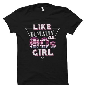 May include: Black t-shirt with a white graphic design that says "Like Totally an 80s Girl" in a retro font.