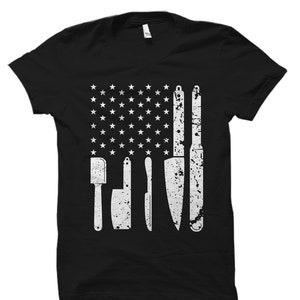 May include: Black t-shirt with a white distressed American flag design featuring a spatula and knives.