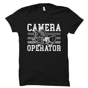 May include: Black t-shirt with a white graphic of a vintage film camera and the text "CAMERA OPERATOR" in a varsity style font.