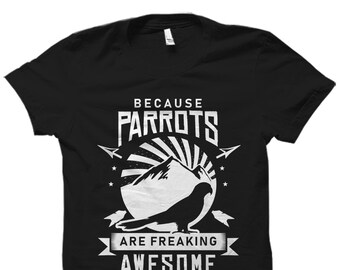 Può includere: T-shirt nero con un design grafico bianco che dice "Because parrots are freaking awesome". La grafica presenta una silhouette di pappagallo, una montagna e un'esplosione di sole.