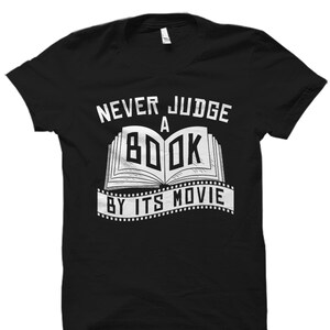 May include: Black t-shirt with white text that reads "Never judge a book by its movie". The text is surrounded by a film strip design.