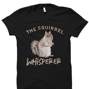 May include: Black t-shirt featuring a brown squirrel illustration and the text "The Squirrel Whisperer" in a beige font.