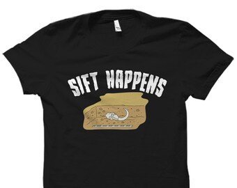 May include: Black t-shirt with a white graphic of a cartoon mammoth skeleton with the text "Sift Happens" in white.